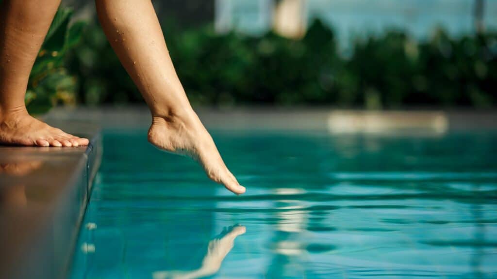 Nahaufnahme junges weibliches Bein berührt blaues Wasser im Schwimmbad