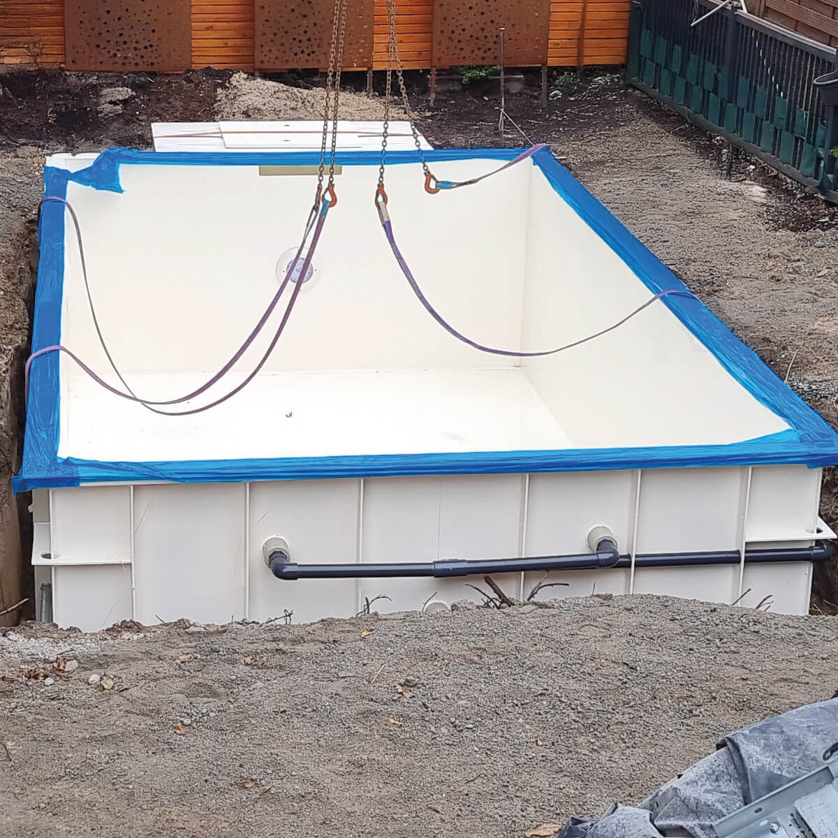 Ein rechteckiger, weißer Pool wird in eine Grube eingelassen; umgeben von Erde und Bauarbeiten.