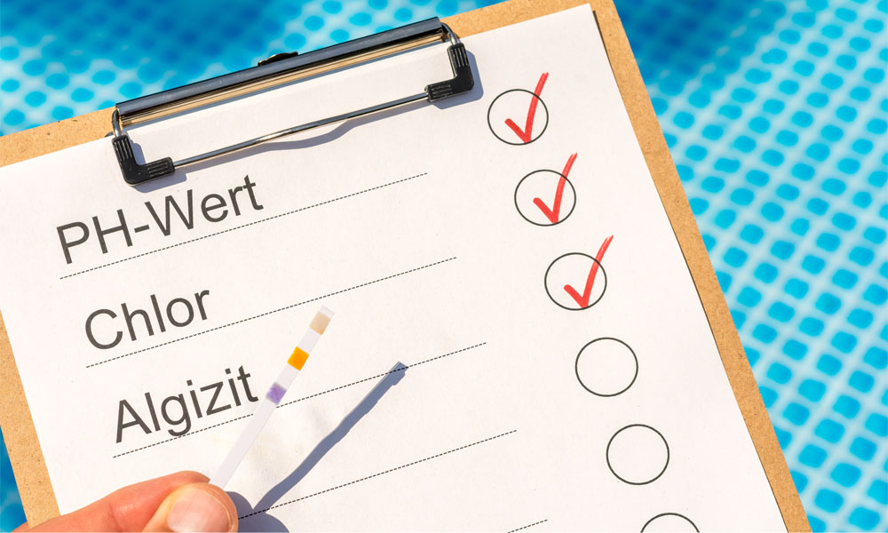 Klemmbrett mit Markierungen und Teststreifen für Poolwasseranalyse vor blauem Hintergrund.