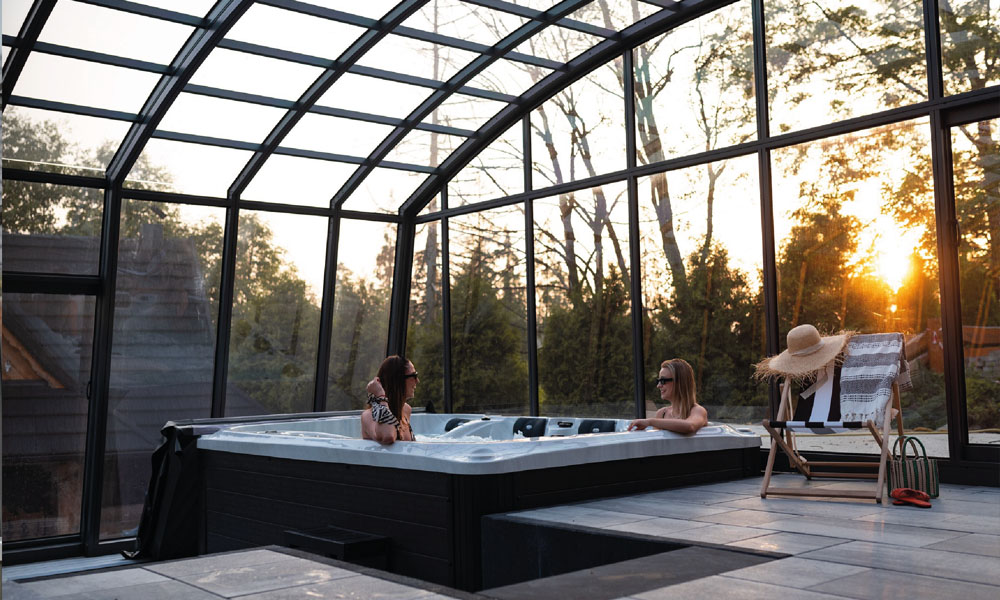 Zwei Personen in einem Whirlpool in einem Wintergarten bei Sonnenuntergang, entspannte Atmosphäre.