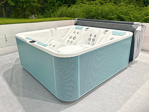 Ein blau-weißes Whirlpool im Freien, umgeben von grünen Bäumen und grauem Bodenbelag.